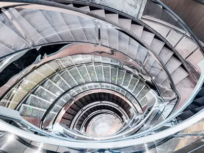 Vogelperspektive auf die spiralförmige, glitzernde Swarovski-Treppe an Bord der MSC Grandiosa, umgeben von geschwungenen, polierten Geländern. Die Treppe reicht über mehrere Decks nach unten.
