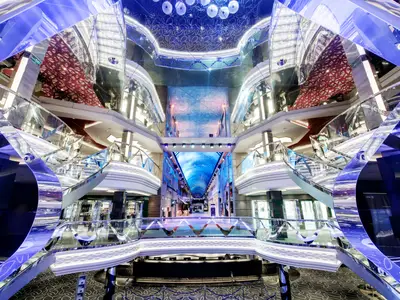Das beeindruckende, mehrstöckige Atrium der MSC Grandiosa zeigt geschwungene Treppen, glänzende Oberflächen und eine lange Promenade mit einer sternenübersäten LED-Decke. Helles, modernes Interieur ohne Personen.