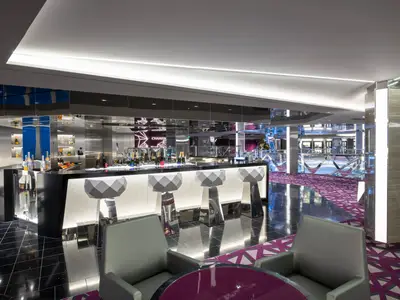 Eine luxuriöse Champagne Bar an Bord der MSC Grandiosa. Sie verfügt über eine beleuchtete Theke, facettierte Barhocker und eine Decke mit Spiegelflächen, die den Raum reflektieren. Flaschen mit Getränken sind auf der Theke zu sehen.