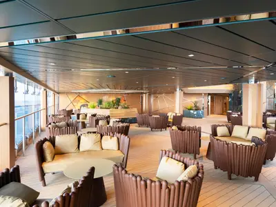 Die Safari Bar Lounge an Bord der MSC Grandiosa. Moderne Sitzgruppen in Braun und Beige. Fenster zeigen Meerblick. Pflanzen und Wandbilder schaffen ein elegantes Ambiente.
