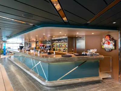 Ansicht der Safari Bar an Bord der MSC Grandiosa. Eine lange, geschwungene Bar-Theke mit Holz- und Glasakzenten, dahinter Regale voller Spirituosen und ein beleuchtetes Safari-Logo.