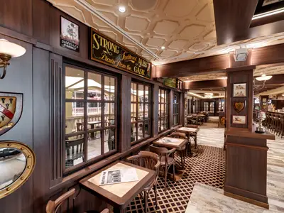 Innenansicht des Masters of the Sea Pub auf der MSC Grandiosa. Zahlreiche Holztische und Stühle verteilen sich in der Bar mit dunkler Holzvertäfelung und einem Deckenrelief. Ein langer Bartresen ist im Hintergrund sichtbar.