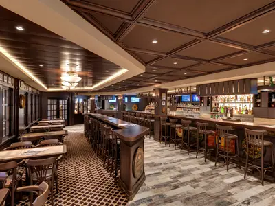 Die Masters of the Sea Bar an Bord der MSC Grandiosa, ein traditioneller Pub mit langer Bar, Barhockern, Tischen und Fensterplätzen. Dunkle Holzvertäfelung und warme Beleuchtung prägen das Ambiente.