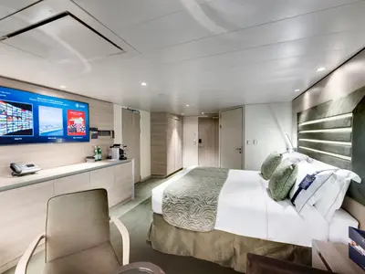 Helle Suite an Bord der MSC Grandiosa mit großem Doppelbett, einem Flachbildfernseher und einer Kaffeemaschine auf einer Kommode. Modernes Design.