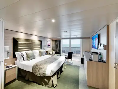 Eine helle, moderne Balkonsuite an Bord der MSC Grandiosa mit großem Doppelbett, Sofa, TV-Bereich und einem Balkon mit Blick auf das offene Meer.