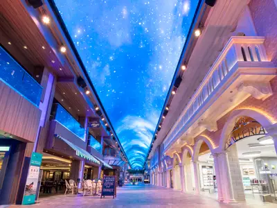 Blick in die elegante Galleria Grandiosa an Bord der MSC Grandiosa. Eine schimmernde LED-Decke zeigt einen blauen Sternenhimmel über einer Promenade mit Geschäften und Restaurants.