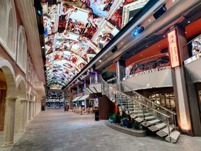 Galleria Grandiosa an Bord der MSC Grandiosa: Helle Promenade mit Arkaden, Geschäften, grossem LED-Himmel, der Kunst zeigt, und eleganter Treppe aus Glas.