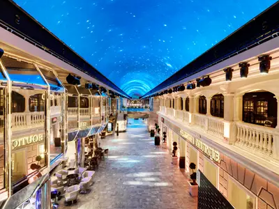 Die helle Galleria Grandiosa auf der MSC Grandiosa. Eine Indoor-Promenade mit Geschäften und Bars, gekrönt von einem funkelnden LED-Himmel mit Sternen.