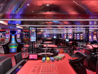 Casino auf der MSC Grandiosa mit Roulette-Tischen voller Chips und leuchtenden Spielautomaten. Rote und violette Lichtstimmung prägt das moderne Ambiente.