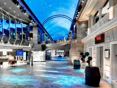 Blick in die beeindruckende Galleria Grandiosa an Bord der MSC Grandiosa, einer langen Indoor-Promenade mit Geschäften, Restaurants und einem animierten LED-Himmel, der den Blick auf Sterne und Galaxien simuliert. Mehrere Sitzgelegenheiten und moderne Elemente sind zu sehen.