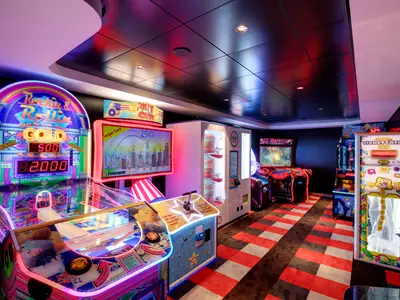 Ein farbenfroher Spielbereich mit mehreren beleuchteten Arcade-Automaten wie Rockin' & Rollin' und einem Preis-Hub an Bord der MSC Grandiosa. Der Boden hat ein rot-graues Schachbrettmuster.