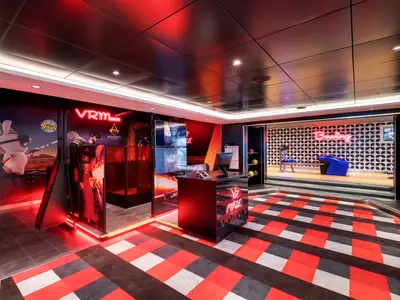 Moderner VR Maze und Bowlingbereich an Bord der MSC Grandiosa. Rote Neonlichter illuminieren die Spielstationen und den rot-schwarz gemusterten Teppich. Eine helle Bowlingbahn ist im Hintergrund. Der Bereich ist ohne Personen.