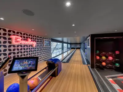 Geräumige Bowlingbahn an Bord der MSC Grandiosa, beleuchtet mit Neonlicht und großen Fenstern mit Blick nach draußen. Bunte Bowlingkugeln sind in einem Regal zu sehen.