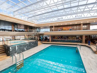 Blick auf den grosszuegigen Safari Pool Bereich an Bord der MSC Grandiosa. Ein grosser Pool, ein Whirlpool und eine Bar befinden sich unter einem lichtdurchfluteten Glasdach.
