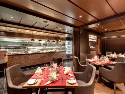 Blick in das elegant beleuchtete Steakhouse 'Butcher's Cut' an Bord der MSC Grandiosa mit gedeckten Tischen und offener Küche.