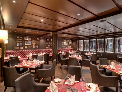 Spezialitätenrestaurant Butcher's Cut an Bord der MSC Grandiosa. Rote Lederbänke, dunkle Tische, Stühle, eine beleuchtete Weinwand und viele gerahmte Bilder schaffen ein elegantes Ambiente.
