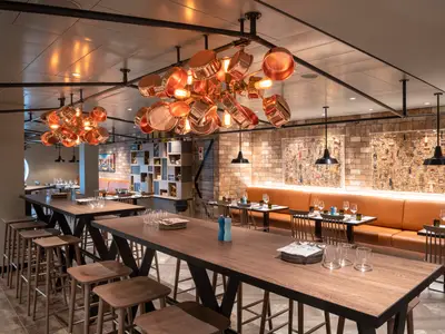 Hola! Tapas Bar an Bord der MSC Grandiosa. Moderne Holztische, hohe Stühle, Lederbänke und Backsteinwände. Kupferpfannen-Kronleuchter beleuchten das stilvolle Restaurant.