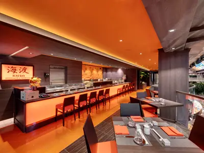 Eine helle, moderne Kaito Sushi Bar an Bord der MSC Grandiosa, dominiert von leuchtendem Orange, mit einer langen Bar, Sitzgelegenheiten und Blick auf das Atrium mit einer bunten Kuppel.