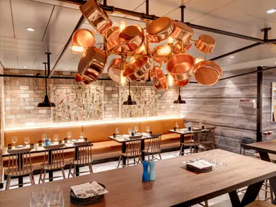Eine moderne Hola! Tapas Bar an Bord der MSC Grandiosa mit markantem Kronleuchter aus Kupfertöpfen, Holztischen und Ledersitzbänken. Ohne Personen.