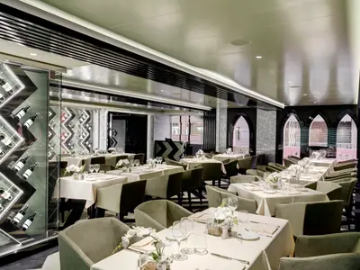 Das elegante Restaurant Il Campo an Bord der MSC Grandiosa zeigt gedeckte Tische, olivgrüne Stühle, moderne Weindisplays und stilvolle Fensterbögen. Keine Personen.