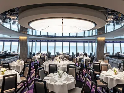 Elegantes Restaurant 'La Loggia' an Bord der MSC Grandiosa mit zahlreichen gedeckten Tischen. Große Panoramafenster bieten weiten Meerblick. Eine ovale Deckenleuchte und moderne Säulen prägen das Interieur.