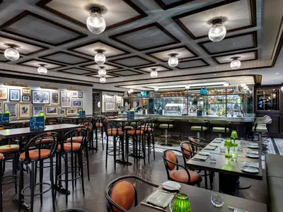 Elegantes L'Atelier Bistrot an Bord der MSC Grandiosa mit langer Bar und zahlreichen Tischen. Wände mit Kunstwerken, Decke mit markanten Lampen. Ohne Personen.