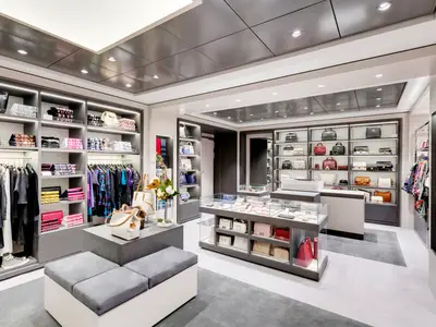 Eine helle, moderne Boutique an Bord der MSC Grandiosa präsentiert Luxus-Handtaschen, Kleidung und Accessoires in eleganten Regalen und beleuchteten Vitrinen. Der Raum ist menschenleer.