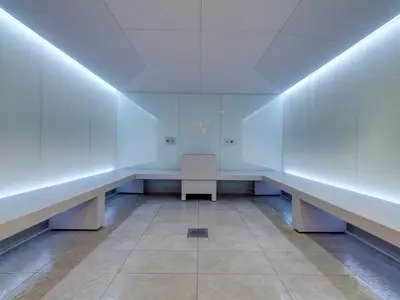 Ein heller, minimalistischer Thermalbereich im MSC Aurea Spa an Bord der MSC Grandiosa mit weissen Bänken, Wänden und Deckenbeleuchtung. Der Boden ist gefliest, mittig ist ein Abflussrost zu sehen.