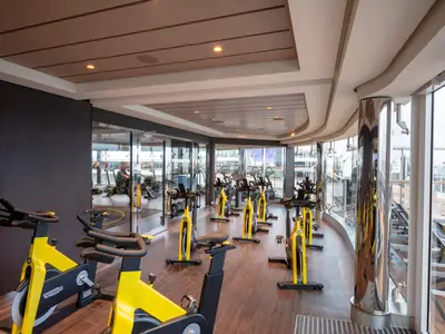 Ein geräumiger Fitnessraum mit vielen gelben Technogym-Spinning-Rädern und großen Panoramafenstern mit Blick auf das Außendeck an Bord der MSC Grandiosa.