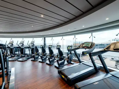 Ein modernes Fitnessstudio an Bord der MSC Grandiosa mit Technogym-Laufbändern und Ergometern. Große Fenster bieten einen weiten Blick auf das Meer und das Außendeck.