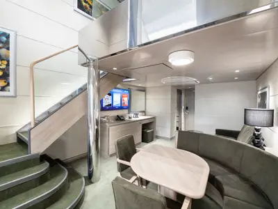 Die zweistöckige Duplex Suite der MSC Grandiosa präsentiert einen stilvollen Wohnbereich mit Sofa, Esstisch, TV und einer Holztreppe.