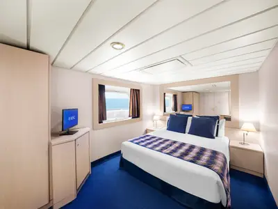 Helle Aussenkabine an Bord der MSC Lirica mit Doppelbett, blauen Kissen, kariertem Überwurf. Kleiderschrank, TV, Meerblick-Fenster. Modern und gemütlich.