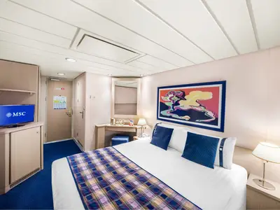 Helle, modern eingerichtete Balkonkabine an Bord der MSC Lirica mit Doppelbett, blauen Kissen und karierter Decke. Fernseher und Schminktisch sind sichtbar.