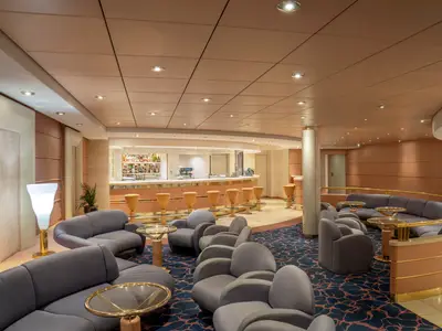 Innenansicht der eleganten Beverly Hills Bar an Bord der MSC Lirica. Eine geschwungene Bar mit Hockern und gemütliche Lounge-Sessel und Sofas auf blauem Teppich sind beleuchtet.