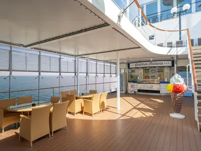Gelateria Italiana auf dem Aussendeck der MSC Lirica. Tische mit Korbstühlen, eine grosse Eistüten-Skulptur und Meerblick kennzeichnen diesen sonnigen Bereich.