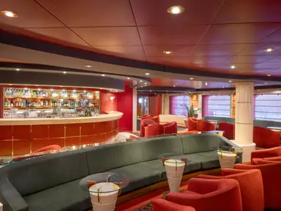 Innenansicht der L'Atmosphere Piano Bar an Bord der MSC Lirica. Geschwungene rote Bar mit Spirituosen und Gläsern. Davor bequeme grüne Sofas, rote Sessel und kleine runde Tische.