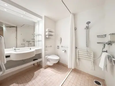 Barrierefreies Badezimmer an Bord der MSC Lirica mit Waschbecken, Toilette und rollstuhlgerechter Dusche. Sichtbar sind Haltegriffe, Duschhocker und Handtuecher.