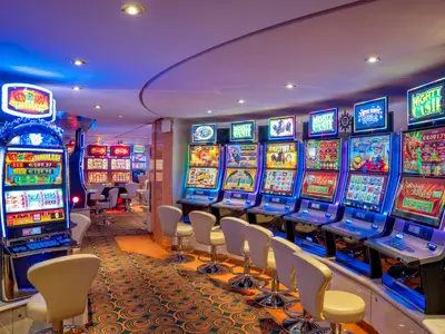 Ein lebhaftes Casino an Bord der MSC Lirica mit zahlreichen bunten Spielautomaten und Stühlen in einer langen Reihe. Die Maschinen leuchten in verschiedenen Farben und zeigen bunte Grafiken. Der Teppich hat ein auffälliges Muster.