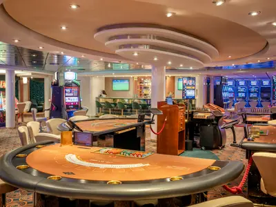 Innenansicht des Las Vegas Casinos an Bord der MSC Lirica. Es zeigt Spieltische, bunte Slotmaschinen und eine elegante Bar mit Hockern. Der Raum ist gut beleuchtet, ohne Personen.