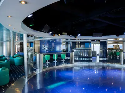 Der Blue Club an Bord der MSC Lirica. Ein moderner Nachtclub mit blauer Tanzfläche, Bar und runden, tuerkisfarbenen Sesseln. Große Fenster bieten Meerblick.
