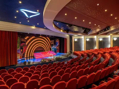 Theater an Bord der MSC Lirica. Rote Samtsitze, eine hell beleuchtete Bühne mit Broadway-Kulisse und Podest. Die Decke zeigt eine Sternenlicht-Installation.