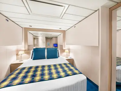 Blick in eine gemütliche Innenkabine der MSC Lirica. Ein Doppelbett mit blauem Plaid, Nachttische mit Lampen und ein großer Spiegel sind zu sehen.