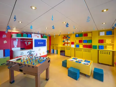 Der helle Kinderbereich der MSC Lirica bietet einen Kicker und Lego-Spieltisch. Bunte Regale mit Bausteinen, musikalische Wandmotive und Segelboote an der Decke.