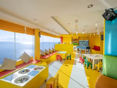 Der helle, farbenfrohe Junior Club der MSC Lirica. Grosse Fenster bieten Meerblick. Mit Legotischen, bunten Stühlen, Tischkicker und Sitzbänken.