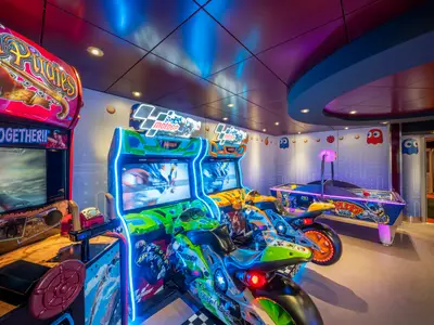 Die lebhafte Spielhalle der MSC Lirica zeigt Moto GP-Videospielautomaten, einen Piraten-Shooter und einen beleuchteten Airhockey-Tisch. Pac-Man-Geister schmücken die thematische Wandgestaltung.