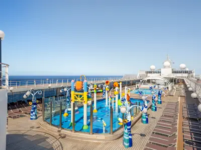 Der bunte Doremi Spray Park an Bord der MSC Lirica unter blauem Himmel. Im Vordergrund sind Wasserspiele, im Hintergrund ein Pool, Liegestühle und das offene Meer zu sehen.