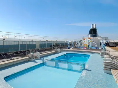Ein weitläufiger Poolbereich an Bord der MSC Lirica mit zwei Pools, einem Wasserspielpark für Kinder und zahlreichen Liegestühlen unter strahlend blauem Himmel. Das Schiff ist von Meer umgeben.