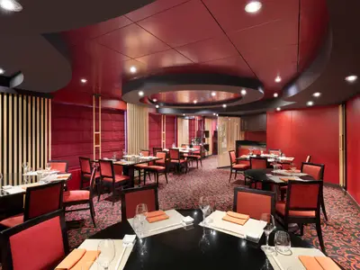 Elegantes rotes Interieur der Kaito Sushi Bar an Bord der MSC Lirica. Gedeckte dunkle Tische, moderne Holzlamellen und stimmungsvolle Deckenbeleuchtung prägen das Ambiente. Keine Personen.