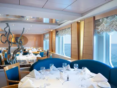 Das Restaurant L'Ippocampo an Bord der MSC Lirica zeigt elegant gedeckte Tische, blaue Sitzgelegenheiten und große Fenster mit Meerblick an einem sonnigen Tag.