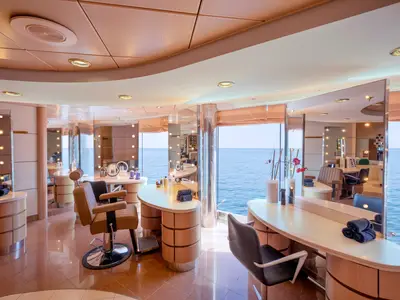 Der elegante Beauty-Salon im MSC Aurea Spa an Bord der MSC Lirica. Er zeigt mehrere Frisierplätze mit Spiegeln und bequemen Stühlen. Große Fenster geben den Blick auf das blaue Meer frei.